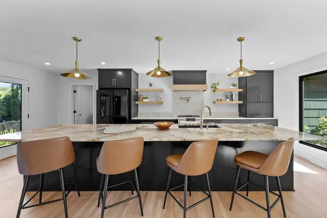 Kitchen by Renovating KC with a black island, quartzite countertop, brass pendant lights and leather counter stools
