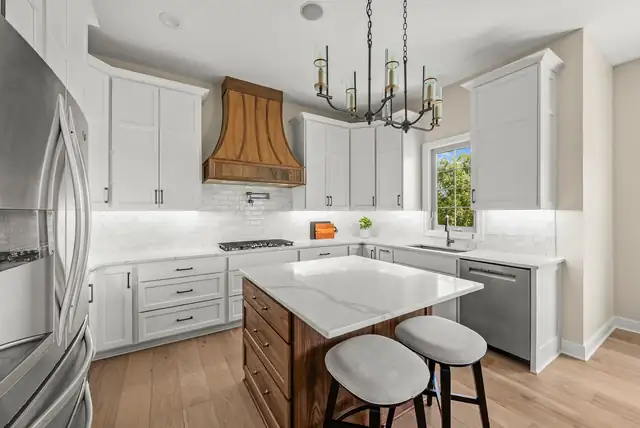 White kitchen with a copper range hood, iron chandelier, wood island and white upholstered stools