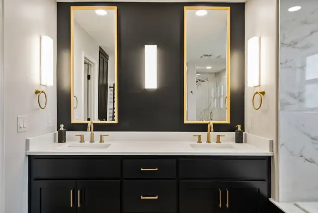 Double vanity with black cabinetry, gold-framed mirrors and brass sconces against a black accent wall