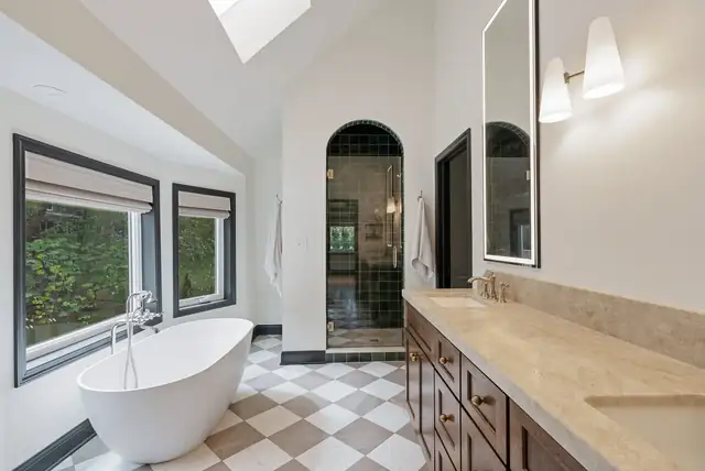 Primary bathroom with a freestanding tub, checkerboard marble floor, wood vanity and arched shower opening under a vaulted ceiling