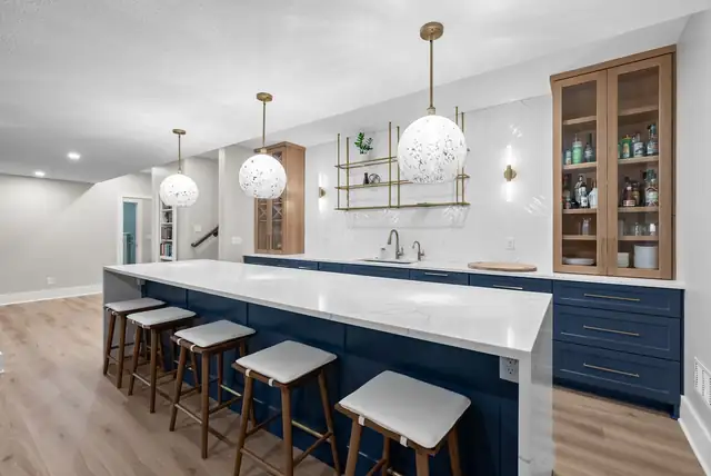 Kitchen with a navy island and white waterfall quartz top, stained wood glass-front cabinets and white globe pendants