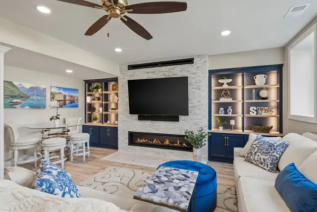 Family room in a Renovating KC remodel with a linear fireplace, stone-look surround and navy built-in shelving