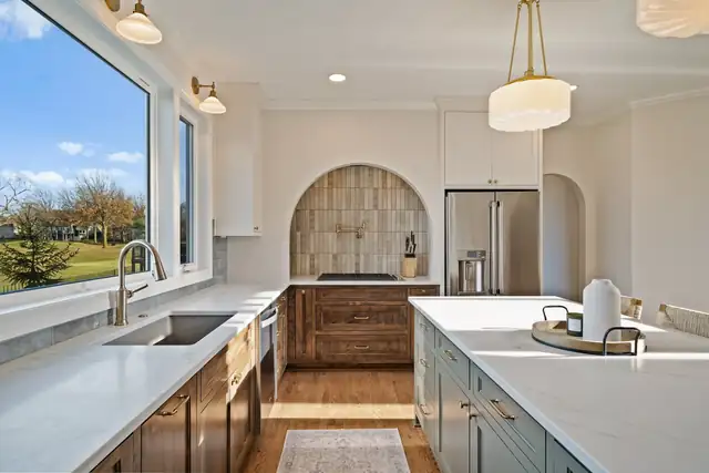 Kansas City kitchen remodel with an arched tile range alcove, stained wood base cabinets, white quartz island and farmhouse sink