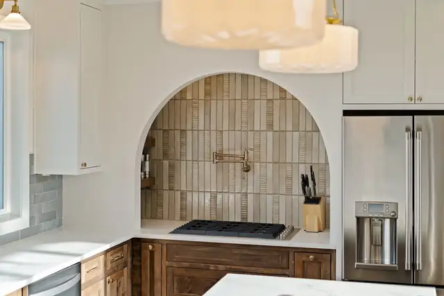 Kitchen with an arched handmade-look tile alcove, pot filler, gas cooktop and white upper cabinets