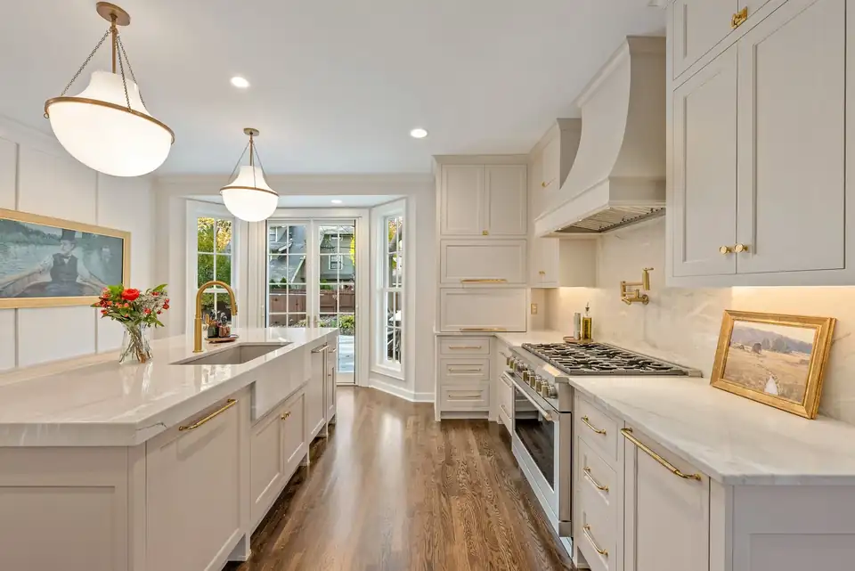 Kitchen remodeling Kansas City: white shaker cabinets, white plaster-style range hood, quartz counters, brass lantern pendants and French doors