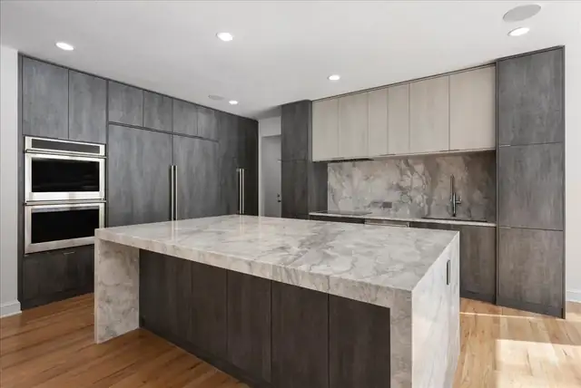 Modern kitchen with charcoal flat-panel cabinets, a marble waterfall island and a full-height marble backsplash