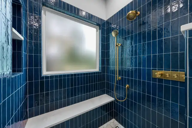 Shower remodel with glossy navy vertical tile, a quartz bench and brushed gold fixtures